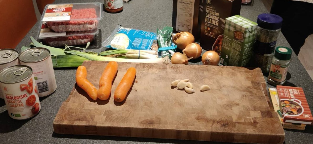 Alle ingridienserne til kødsovs lagt klar på bordet, med et skærebrædt af træ i midten, klar til at snitte grøntsager på.